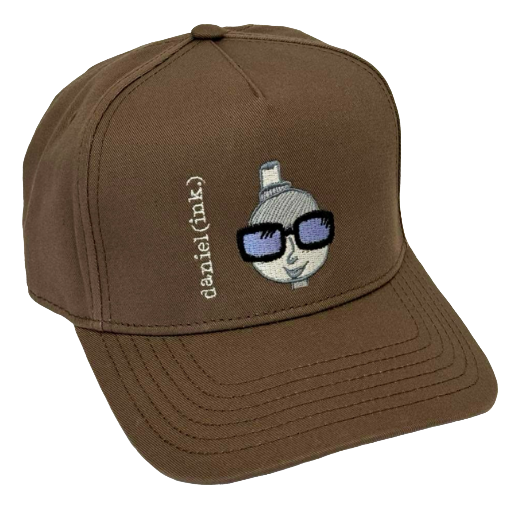 Walnut snapback cap featuring an embroidered image of a person's head in silver. The person is wearing a small top hat and big sunglasses with black frames and blue lenses. The name daniel(ink.) is embroidered in silver thread next to the person's head.
