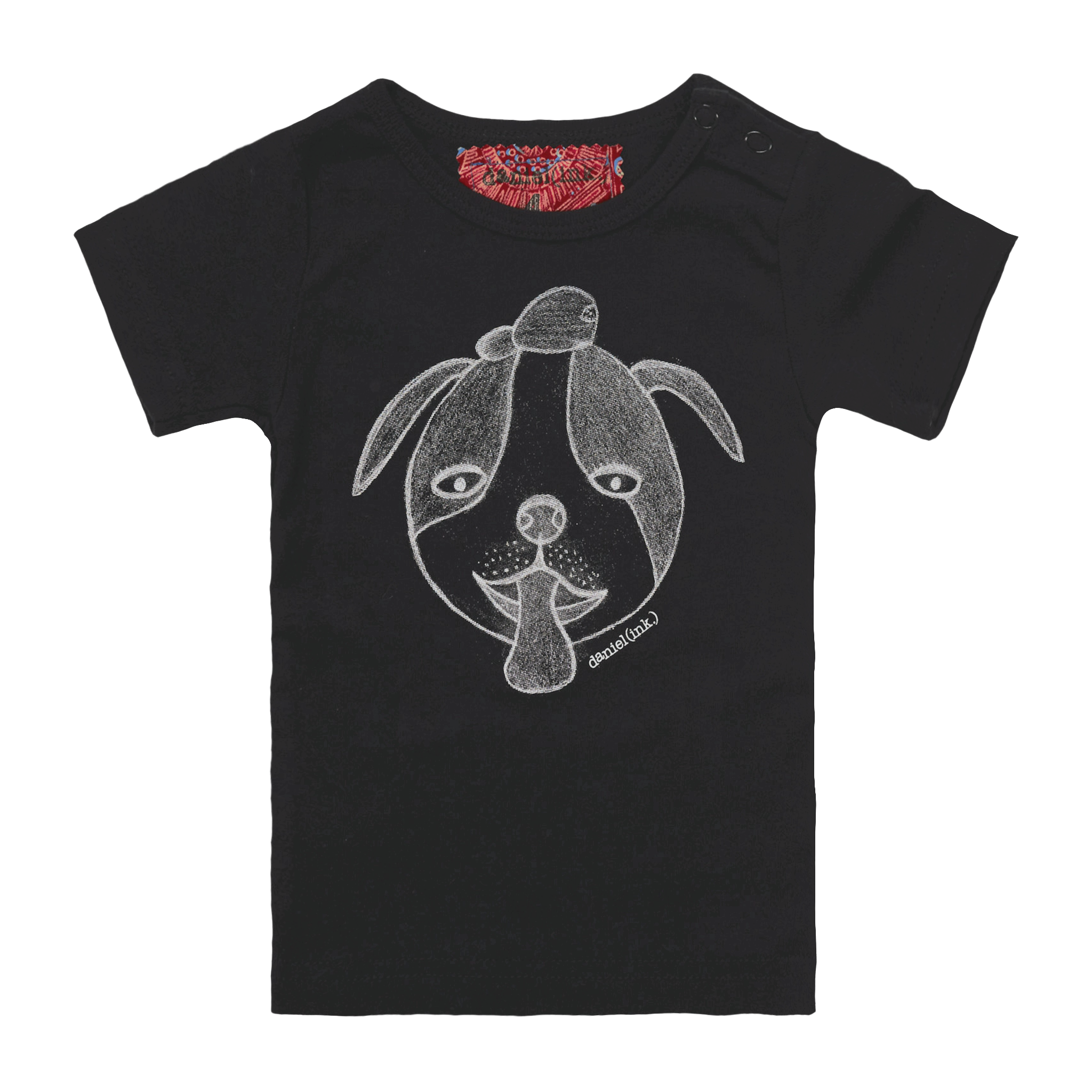 Black short sleeve babies’ t-shirt featuring a hand drawn sketch of a dog’s face in white. The dog has a round head, floppy ears, wide eyes, and its tongue is sticking out. The t-shirt has a red fabric label on the back of the neck and has two black press studs on the left shoulder.