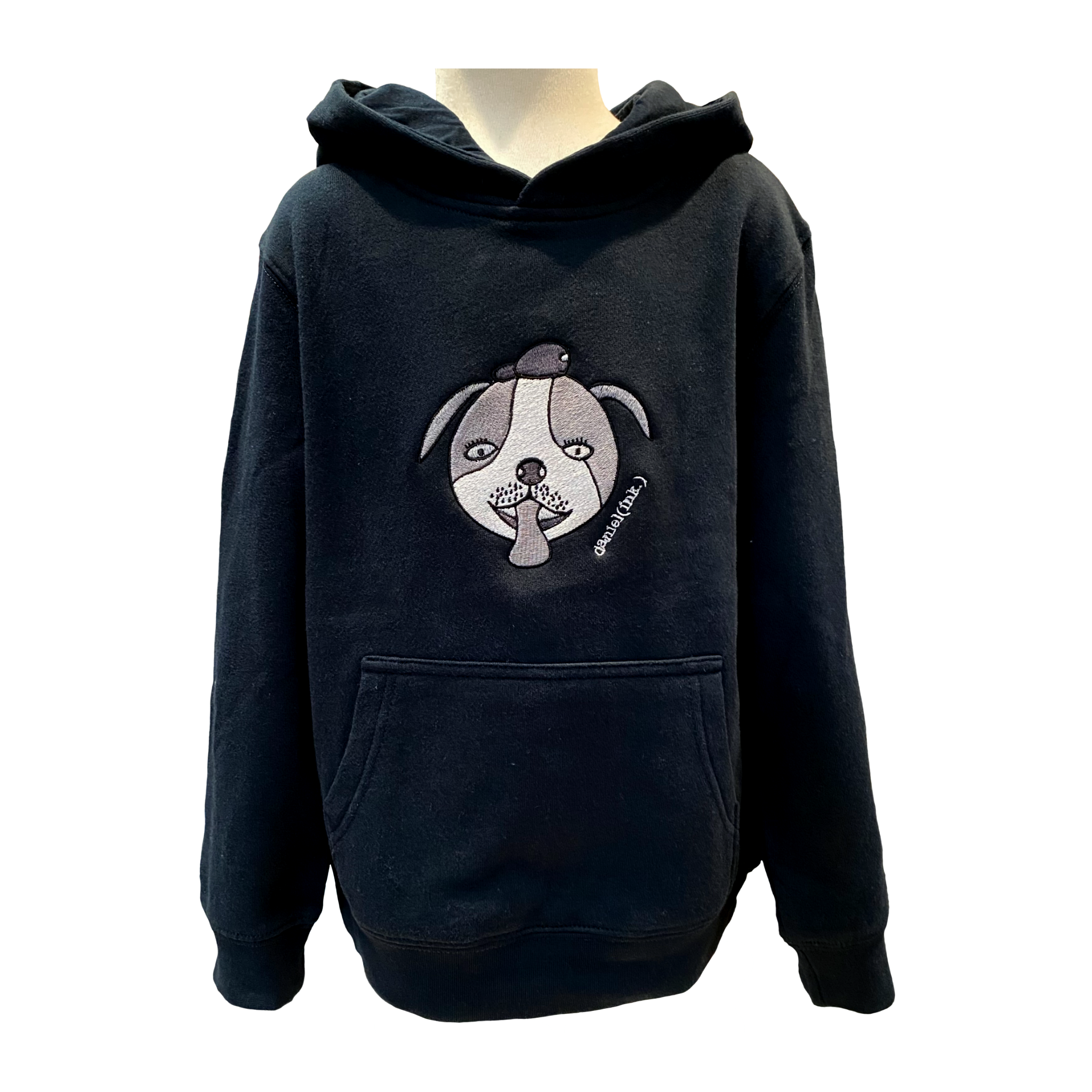 Navy kids' hoodie featuring an embroidered image of a dog’s face in silver. The hoodie features a pullover hood, inset sleeves, and a kangaroo pocket. The embroidered image of a dog's face has a round head, floppy ears, wide eyes, and its tongue is sticking out. The name daniel(ink.) is embroidered in silver thread next to the dog's face. 